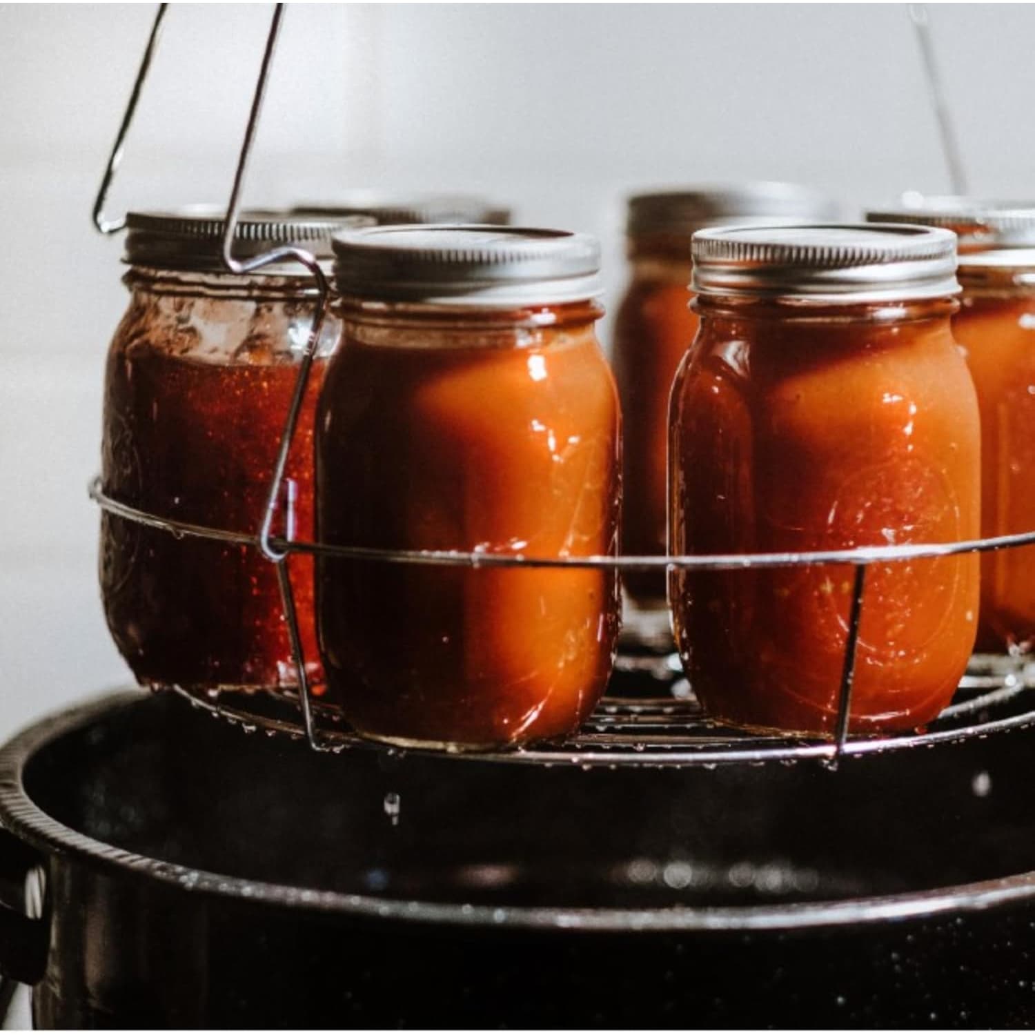 Metal wire rack holding glass jars of preserved food inside a black speckled enamel steel canner pot for home use