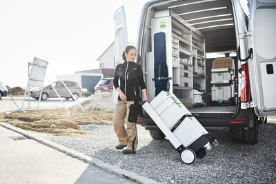 Person moving interlocking Festool tool storage boxes on wheeled cart from van for jobsite organization and home improvement tasks