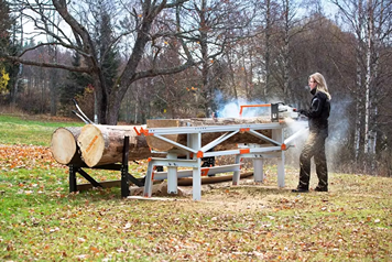 Outdoor scene of a metallic gray and orange chain sawmill with two adjustable log lifts used for wood cutting and home improvement tasks