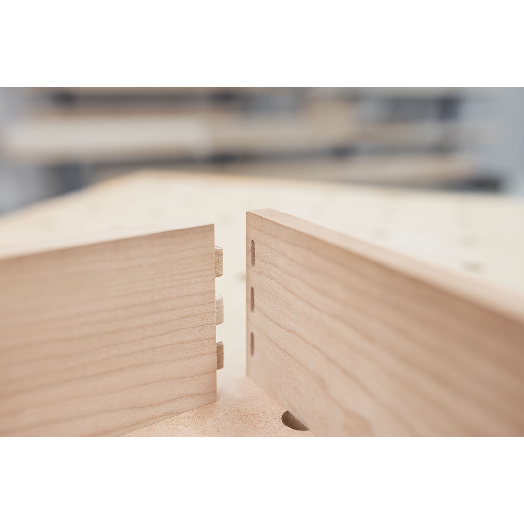 Close-up of two light wood pieces with multiple rectangular mortise joints ready to connect, showcasing woodworking joinery craftsmanship in a workshop setting.