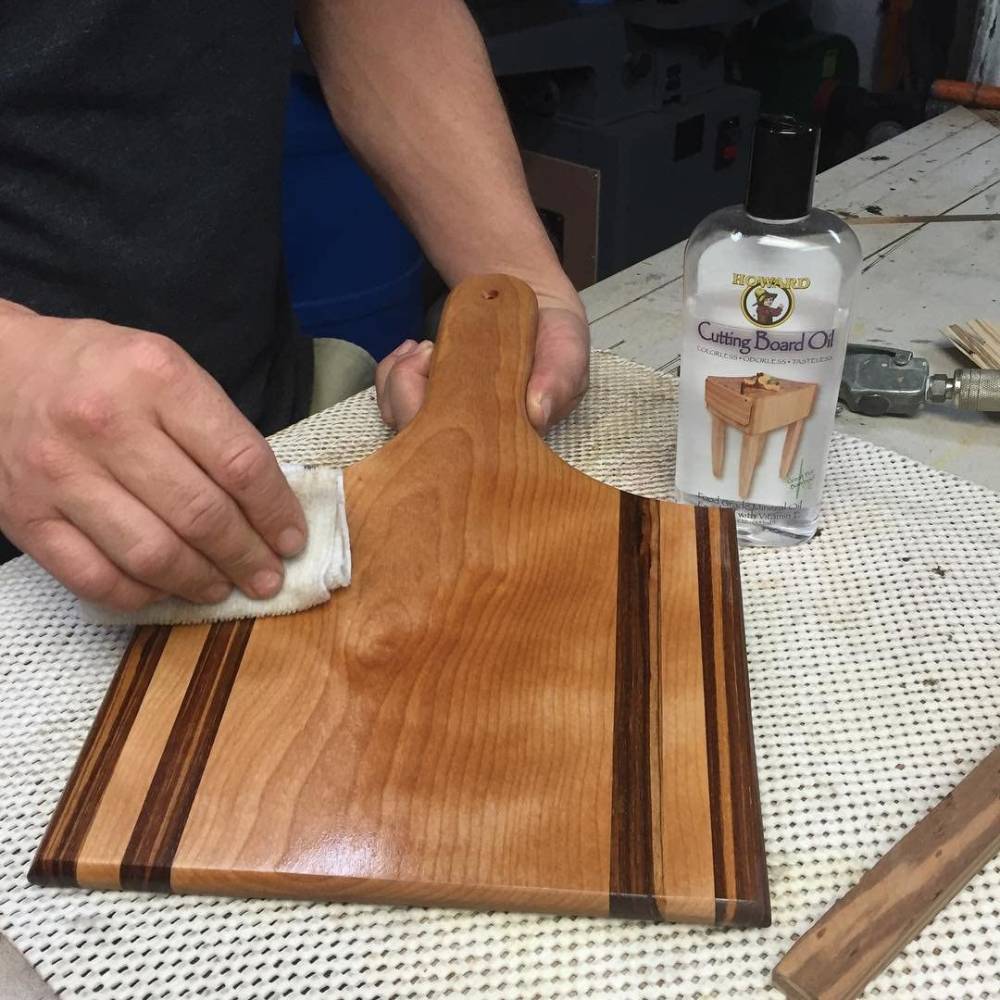Person rubbing Howard Cutting Board Oil onto a wooden cutting board in a home improvement workshop setting