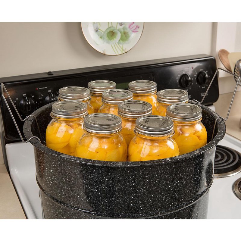 Black speckled graniteware preserving canner filled with glass jars of peaches on stovetop for home use