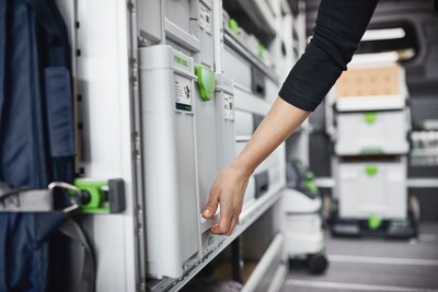 Hand reaching to pull gray and green modular Systainer3 tool storage box from vehicle shelving for workshop organization