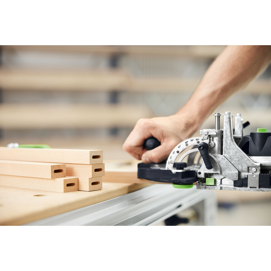 Close-up of a person using a Festool DOMINO joiner to create precise mortise joints on wooden boards in a well-lit woodworking workshop, part of power and woodworking tools collections.