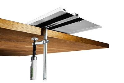 Metal clamp securing an aluminum guide rail to the edge of a wooden workbench in a woodworking setup