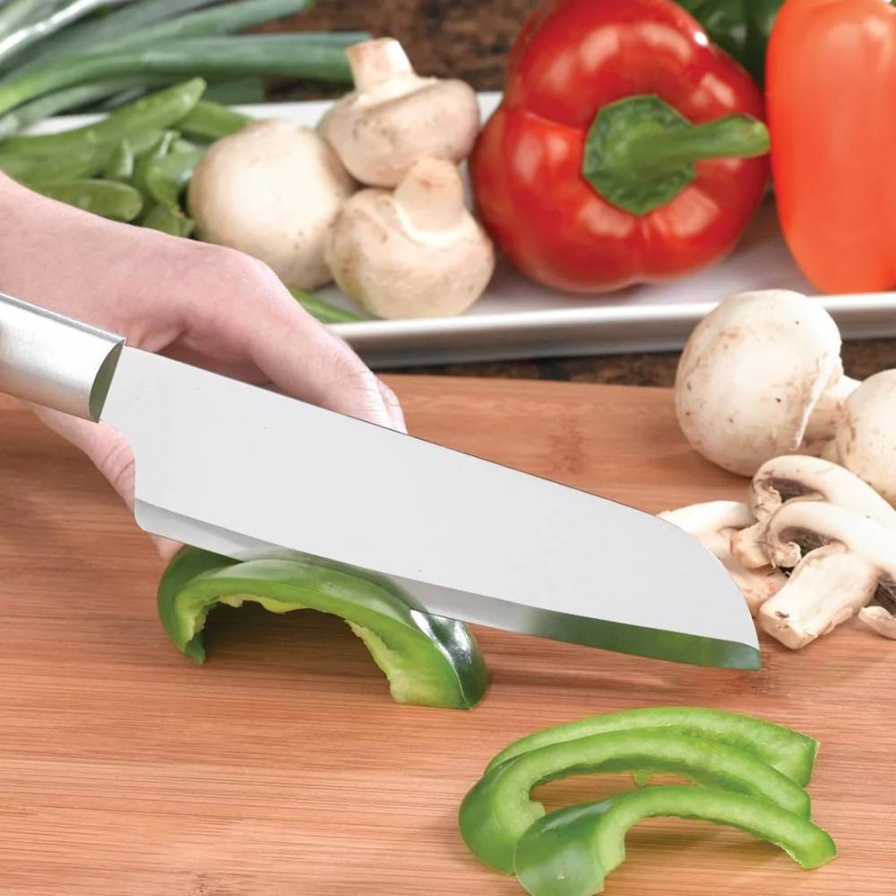 Hand slicing green bell pepper with stainless steel cooks knife on wooden cutting board with mushrooms nearby