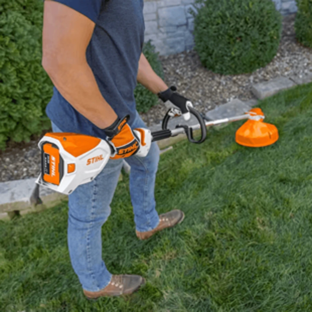 Man using orange and white cordless string trimmer with lithium-ion battery for home improvement outdoor lawn care tasks