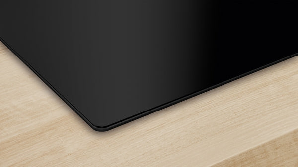 Black-glass seamless electric cooktop corner mounted on a light wood countertop from Bosch appliances collection