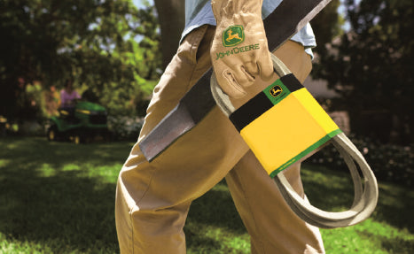 Person wearing branded gloves holding a bundled replacement belt outdoors near a riding mower on a sunny day