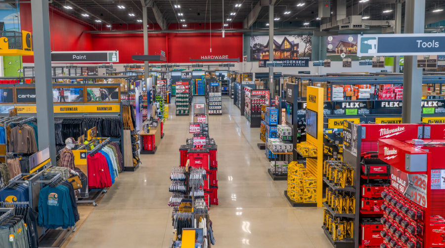 Interior view of a spacious home improvement store aisle featuring organized shelves stocked with tools, hardware, and work apparel.